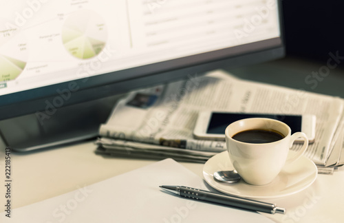 A cup of coffee with newspaper and mobile phone on the desk of a businessman.
