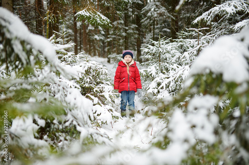 Adorable little girl having fun in beautiful winter forest. Happy child playing in a snow.