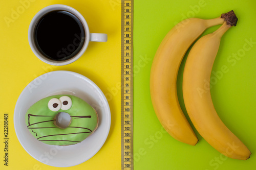 Concept of unhealthy eating and snack. Delicious donut and cup of strong coffee isolated on yellow and fresh tasty bananas isolated on green background. Top view photo photo