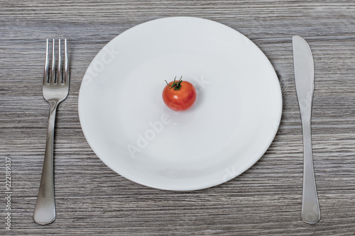 Concept of low-calorie diet. Little cherry tomato on white plate with cutlery