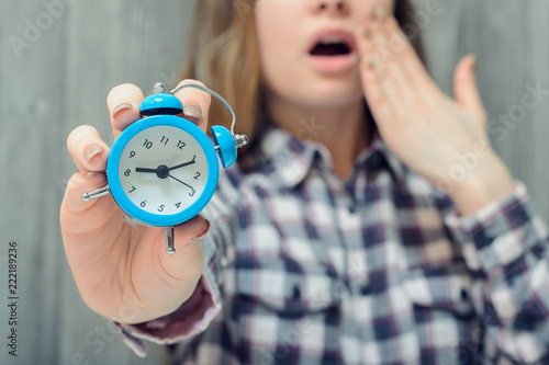 Closeup photo of alarm clock in hand and yawning woman on background