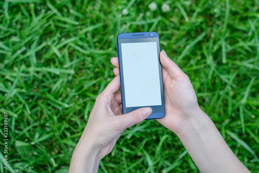 Hands holding mobile phone with empty screen over grass background Hands holding mobile phone with empty screen over grass background