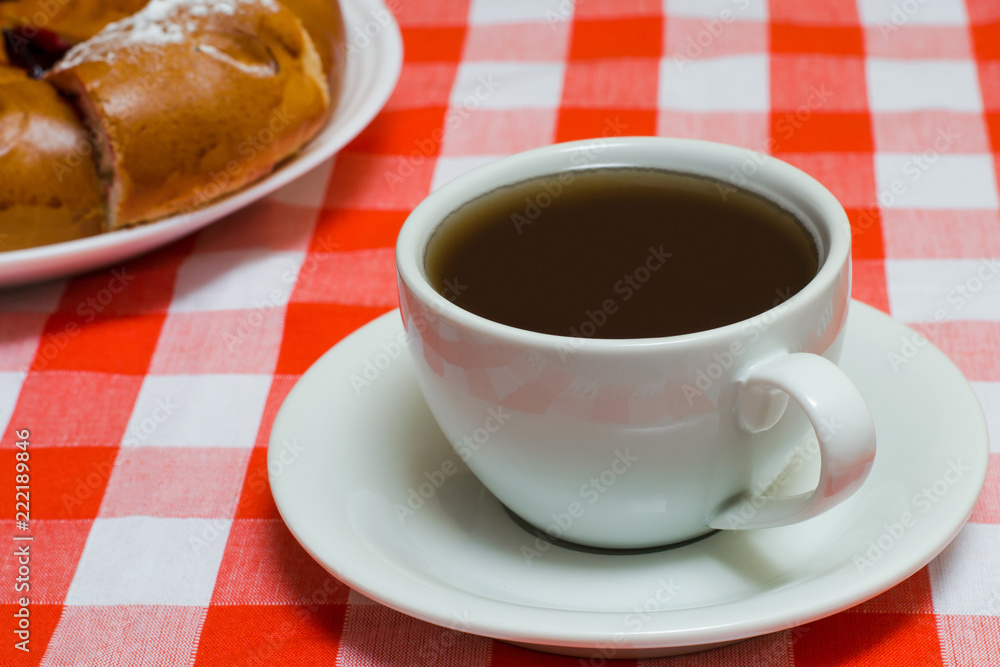Cup of coffee on checkered red tablecloth with cake on the background. Close up photo Cup of coffee on checkered red tablecloth with cake on the background. Close up photo