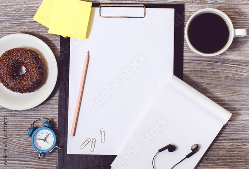 Top view of office accessorise on wooden desktop: clock, cup of coffee, clipboard, donut, notepad and glue stickers photo