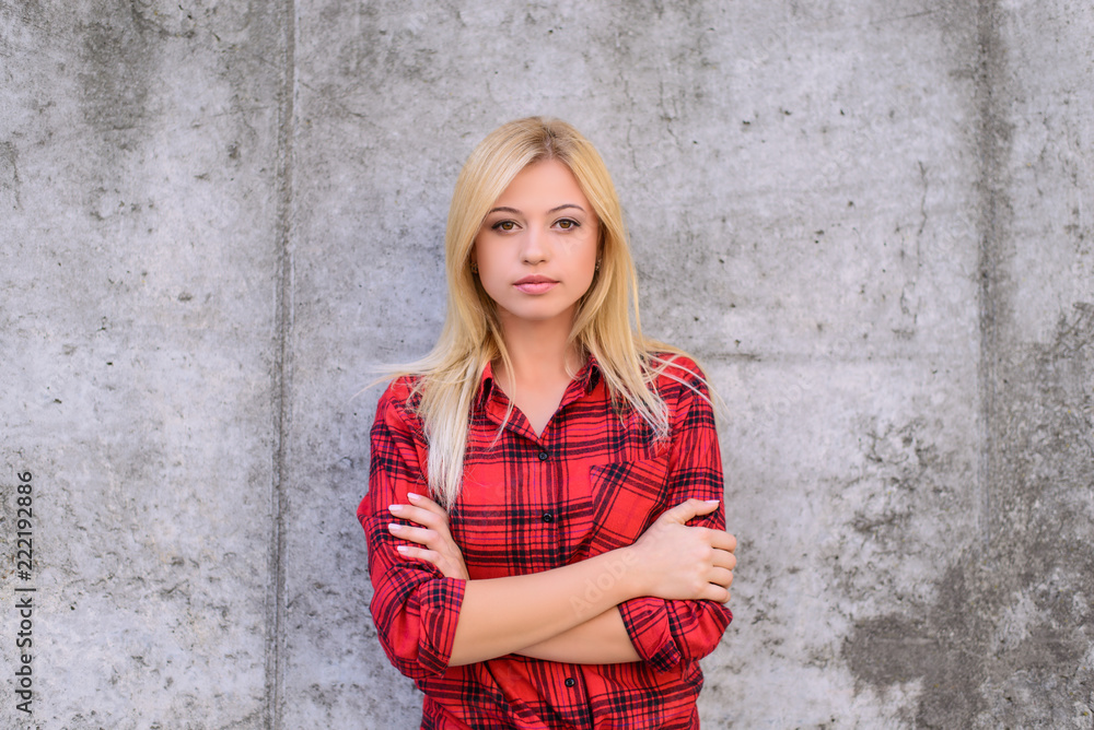 Confident calm woman with crossed arms, looking at camera. Beautiful young girl in checkered red shirt standing against grey background Confident calm woman with crossed arms, looking at camera. Beautiful young girl in checkered red shirt standing against grey background