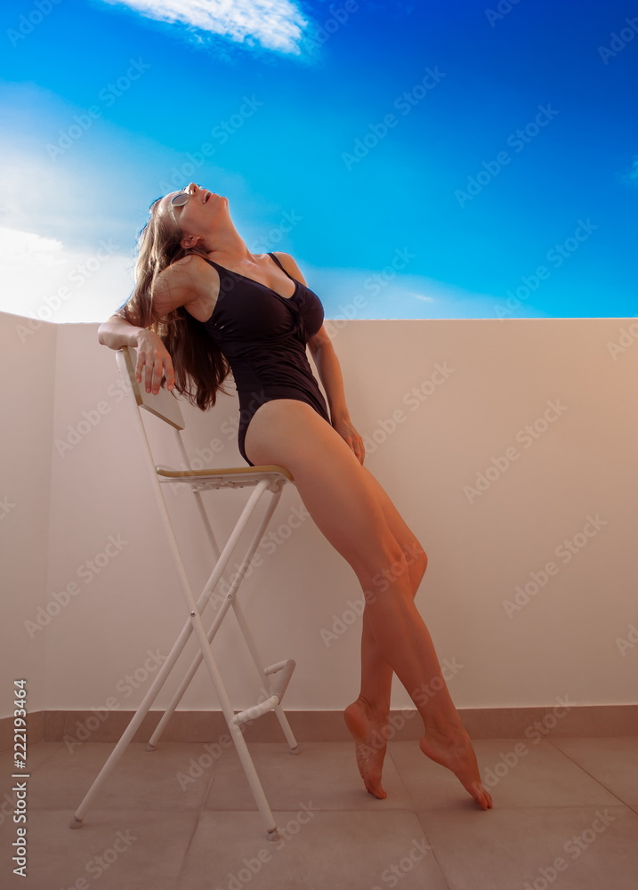 Fototapeta premium Woman in black swimsuit, sits on chair
