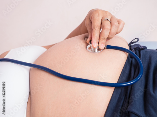 pregnant woman applying ears stethoscope on her belly