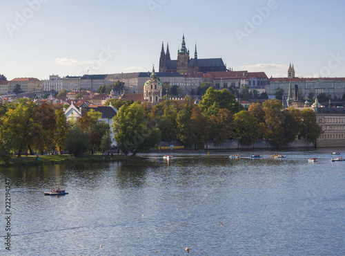 panorama of Prague Castle and St. Vitus Cathedral over Vltava river and Gradchany, Czech Republic, golden hour light, summer sunny day, tourists relaxing on boats photo