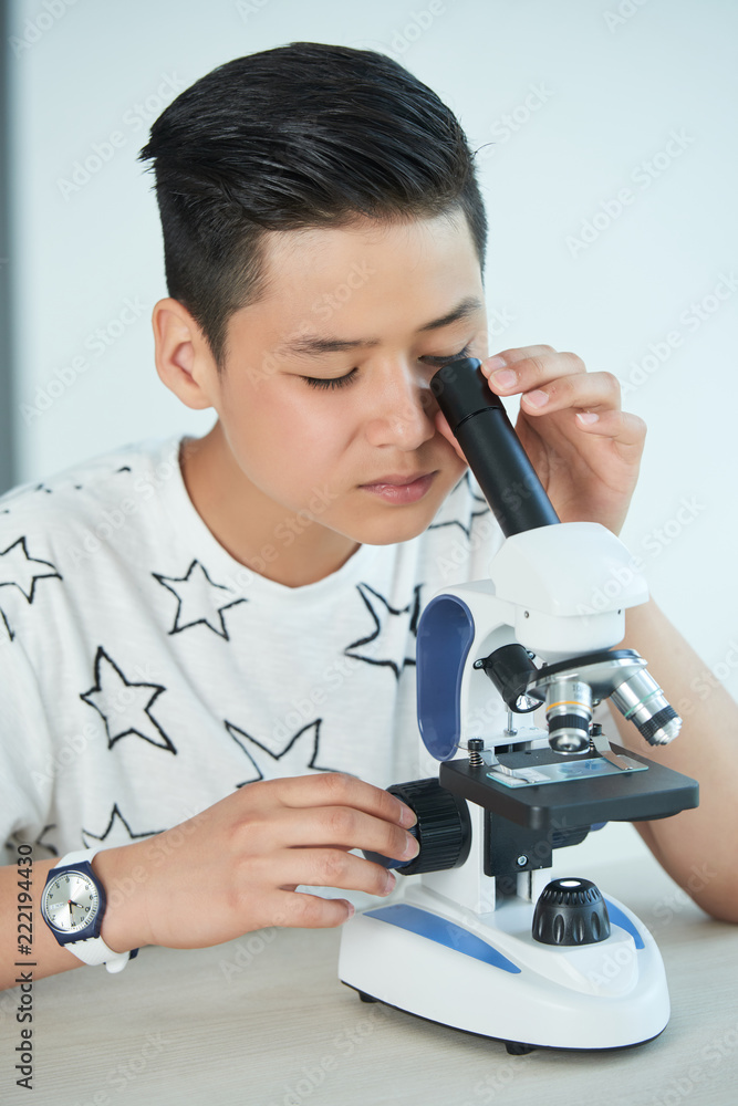 Vietnamese teen boy looking into microscope at biology lesson Vietnamese teen boy looking into microscope at biology lesson