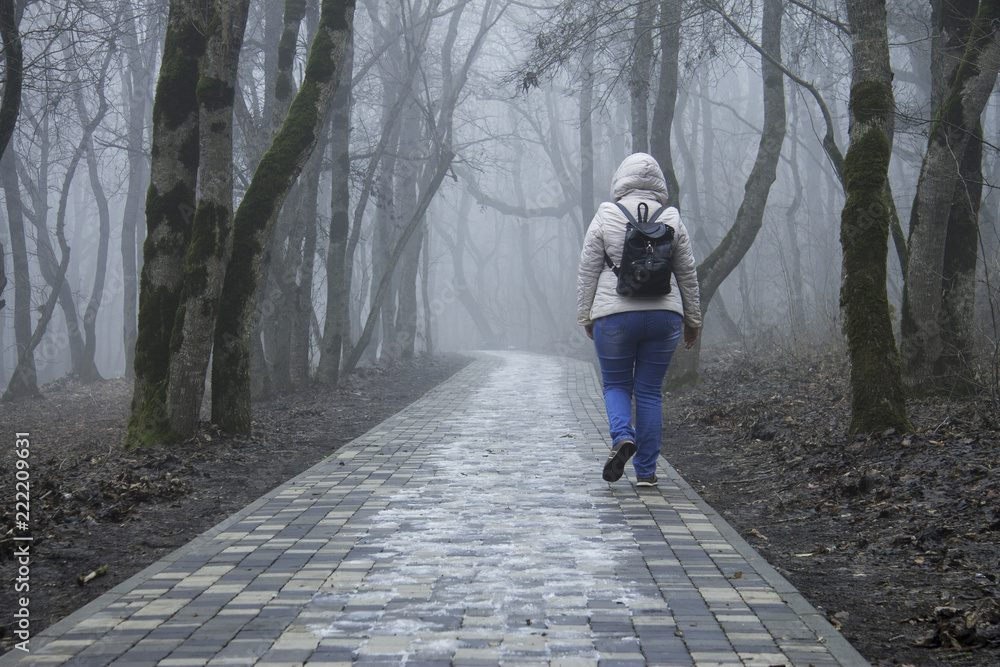 Fototapeta premium Lonely adult woman walking in autumn park in mysty morning