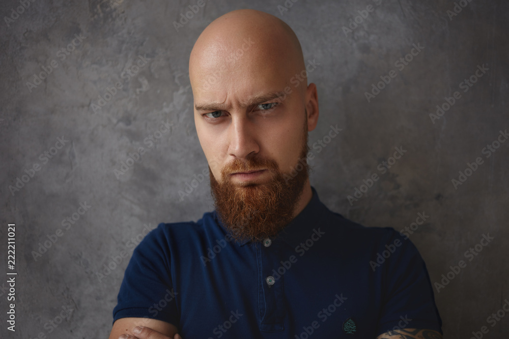 Close up portrait of handsome frowning young bald man with thick beard ...