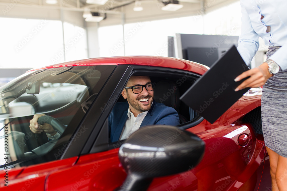 Saleswoman at the dealership showroom talking with customer and helping him to choose a new car for himself. Saleswoman at the dealership showroom talking with customer and helping him to choose a new car for himself.