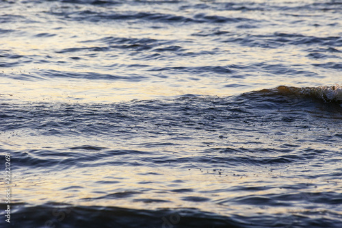 Waves on the sandy shore of a large river. The rays of light are reflected in the waves.