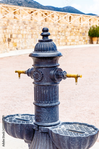 Black fountain for drinking water on the background of stone walls.