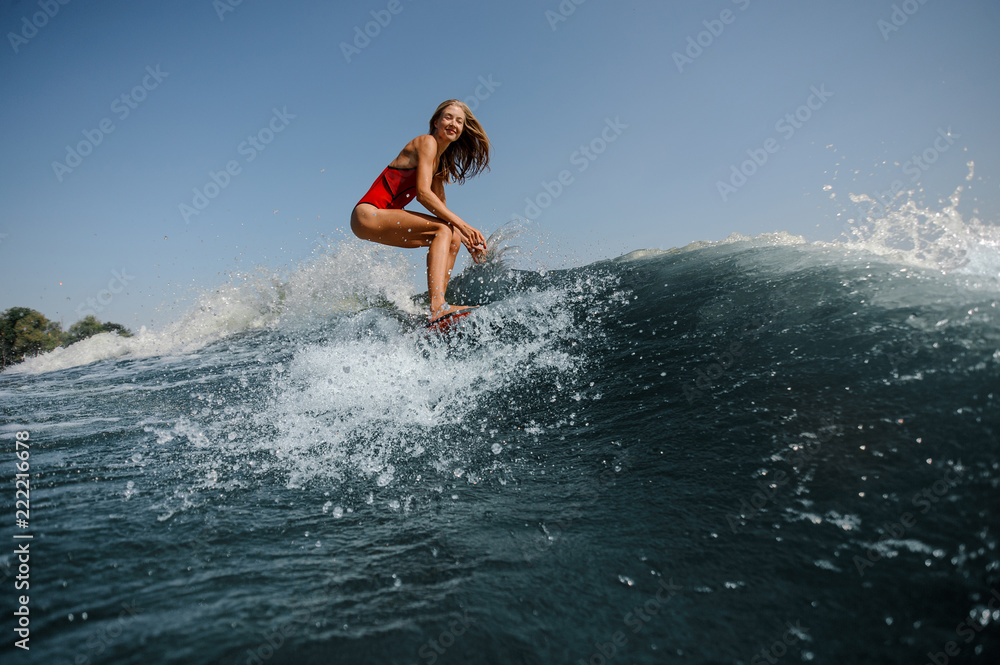 Smiling blonde girl standing on the red wakeboard on the lake