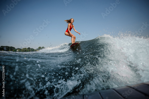 Wave in front of blonde girl riding on the red wakeboard