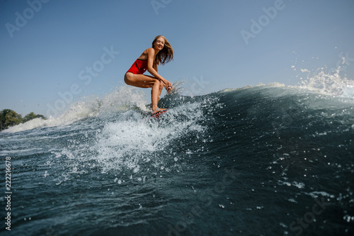 Smiling blonde girl standing on the red wakeboard on the lake