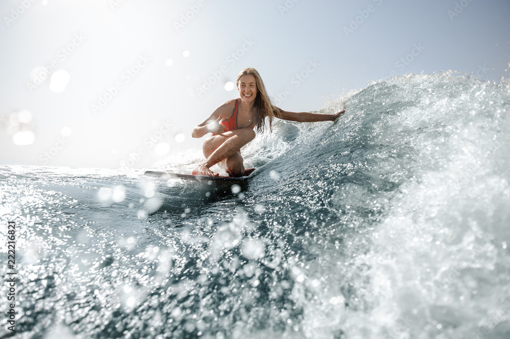 Blonde girl standing on the wakeboard and looking at camera