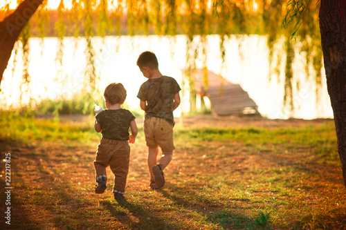two brothers run in the sun to the lake.