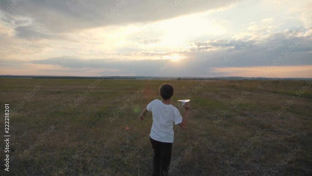 A boy in the field at sunset runs and throws a paper plane. The concept of a happy child A boy in the field at sunset runs and throws a paper plane. The concept of a happy child