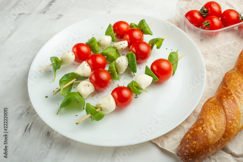 Salad Caprese - shish kebab with tomato, mozzarella and basil, tomatoes and French baguette, Italian cuisine and a healthy vegetarian diet on a light background. with copy space, top view, flat lay