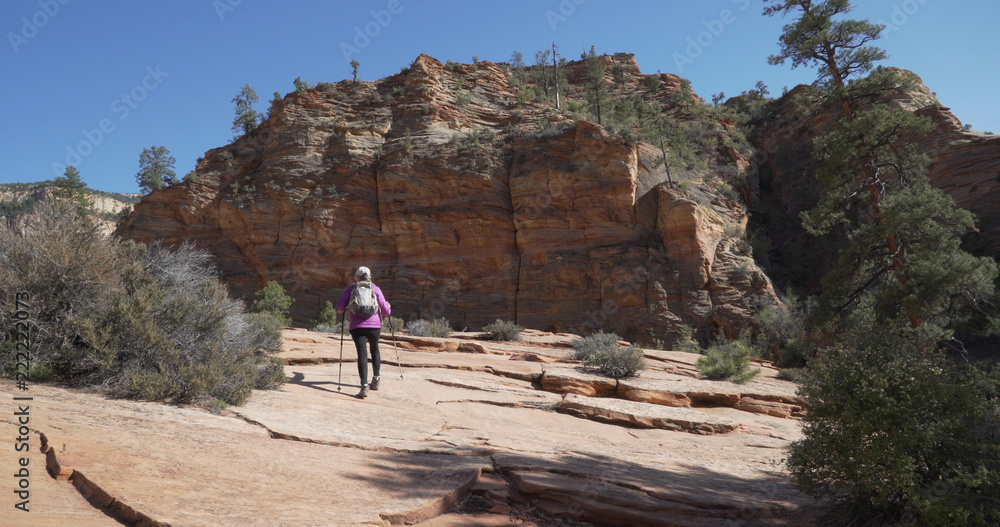 Wide shot of healthy elderly woman hiking towards red sandstone cliff