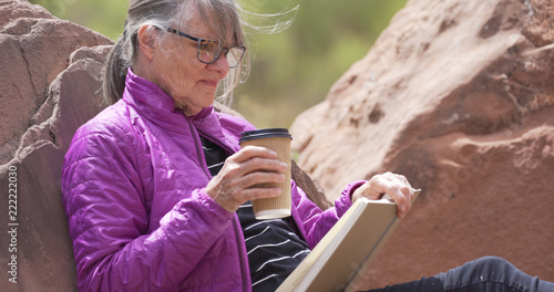 Fényképezés Mature outdoors enthusiast smiling and reading book in nature seated on rock