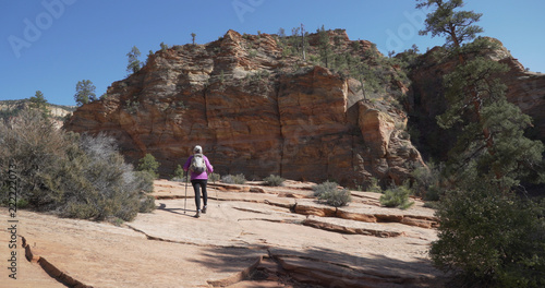 Wide shot of healthy elderly woman hiking towards red sandstone cliff