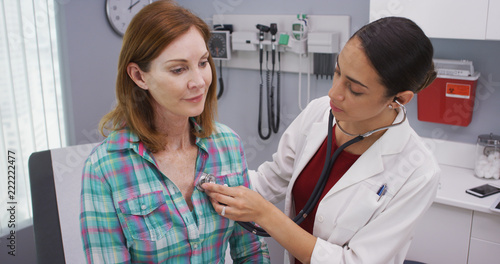 Принти на полотні Lovely young latina doctor using stethoscope to examine senior patients vitals