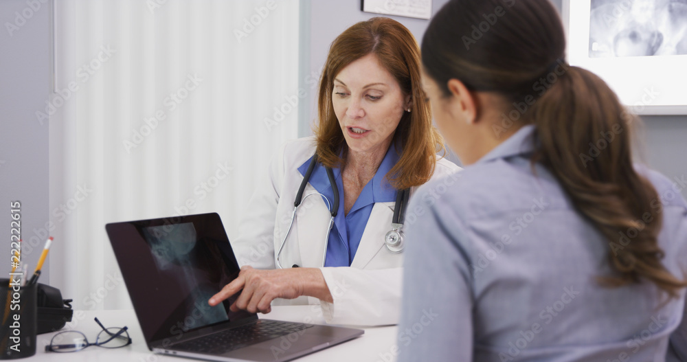 Portrait of senior medical doctor showing xray of spine neck and cranium to young female patient. Close up of young patient consulting with doctor over neck x ray Portrait of senior medical doctor showing xray of spine neck and cranium to young female patient. Close up of young patient consulting with doctor over neck x ray