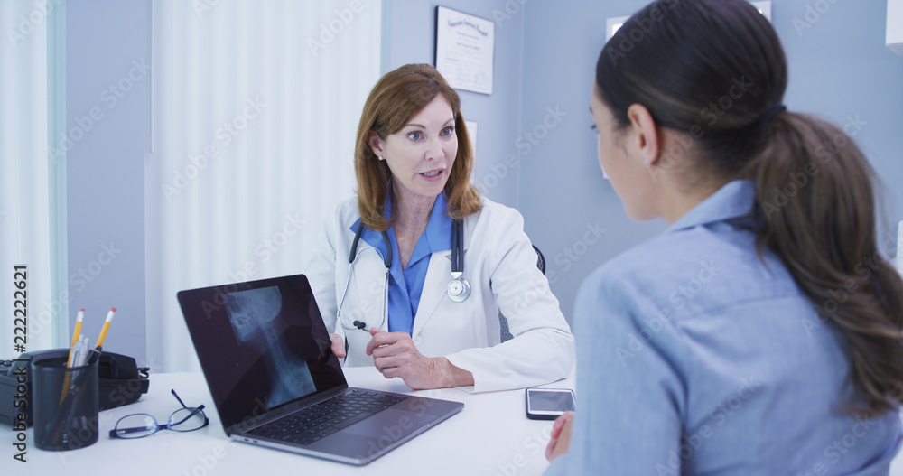 Close up of charming senior doctor discussing results of spine x ray with patient. Portrait of mid aged doctor and young patient looking at laptop computer with spine and skull xrays Close up of charming senior doctor discussing results of spine x ray with patient. Portrait of mid aged doctor and young patient looking at laptop computer with spine and skull xrays