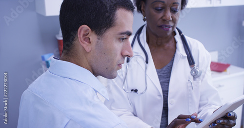 Portrait of black senior medical doctor using notebook tablet to show patient test results. Close up of young male latino patient looking at exam results on portable electronic pad