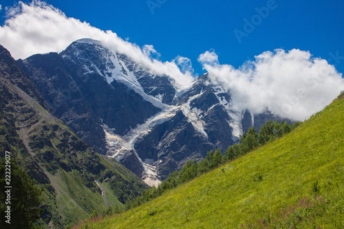 Summer mountain landscape of the North Caucasus. Snow-capped peaks and green grass in the foreground.