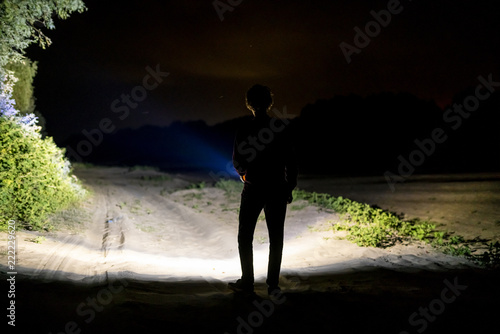 back view of man standing outdoor on night forest road lighting the way with electric flashlight d photo