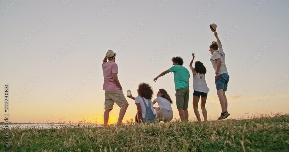 Six teen friends sitting on a meadow shore of a lake , meeting sunset and cheering, having fun 4k Six teen friends sitting on a meadow shore of a lake , meeting sunset and cheering, having fun 4k