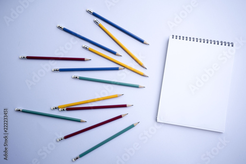 A white notebook with multicolored pencils is placed on a white background.