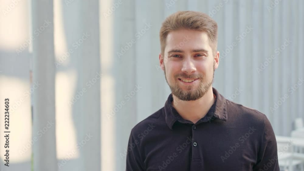 A happy smiling man with a beard standing against a white blurry background. Medium shot. Soft focus A happy smiling man with a beard standing against a white blurry background. Medium shot. Soft focus
