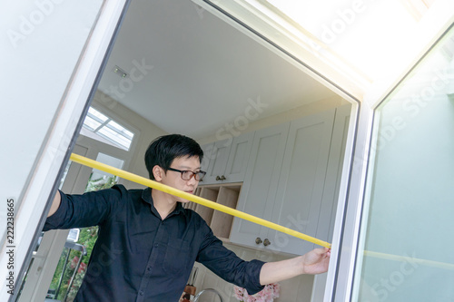 Young Asian worker man using tape measure on door frame in the kitchen. Home interior designer measuring elements on site. Housing design and construction concept
