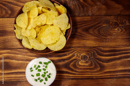 Crispy potato chips with green onion and sour cream on wooden table. Top view