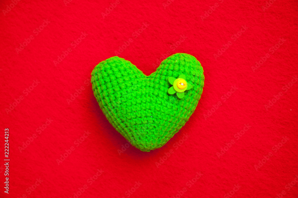 Fototapeta premium green knitted heart on a red background, a symbol of love to congratulate the holiday