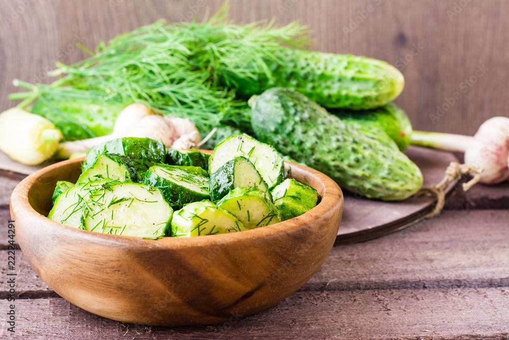 Freshly salted cucumber pickled with garlic and dill in a wooden plate