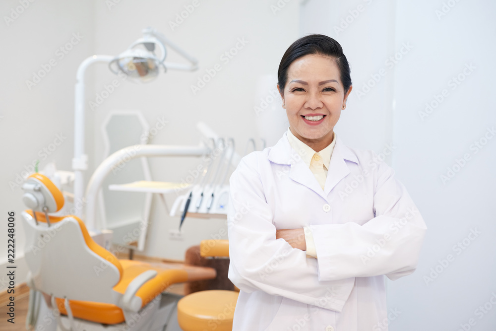 Portrait of female mature doctor in dental clinic folding arms and looking at camera Portrait of female mature doctor in dental clinic folding arms and looking at camera