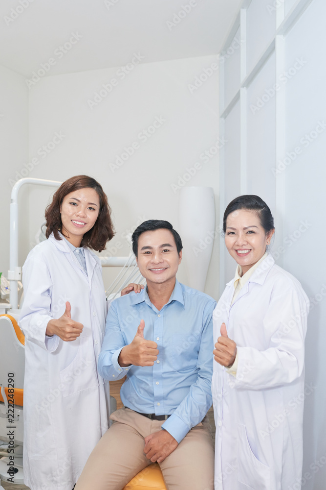 Portrait of cheerful Vietnamese man, dentist and nurse showing thumbs-up