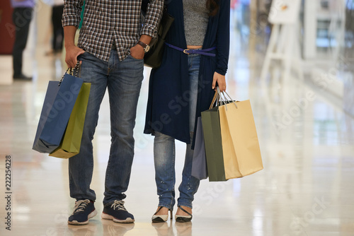 Cropped image of couple with many paper-bags standing in shopping mall
