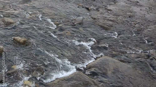 HD video footage showing water slowly flowing on a riverbed with rocks in the way, making whitewater bubbles 