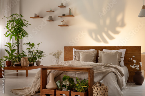 Shadow of a leaf on a wall in a botanical bedroom interior with a comfy double bed. Real photo