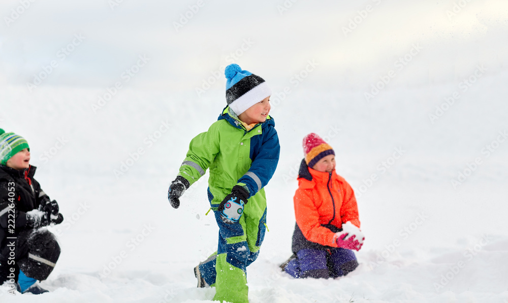 childhood, leisure and season concept - group of happy little kids in winter clothes playing with snow outdoors