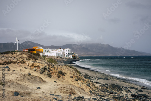 little town on coastline near the waves of the ocean with little houses and caravan and a windmill to produce the electricity they need to surive alone in the middle of nowhere. alternative lifestyle photo