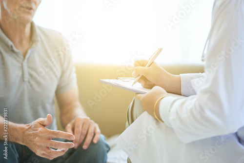 Faceless view of senior man talking to doctor in bright light while taking notes on clipboard