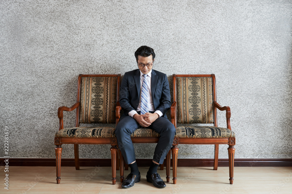 Serious focused Asian man in formal suit sitting on chair looking down in  deep thoughts Stock Photo | Adobe Stock